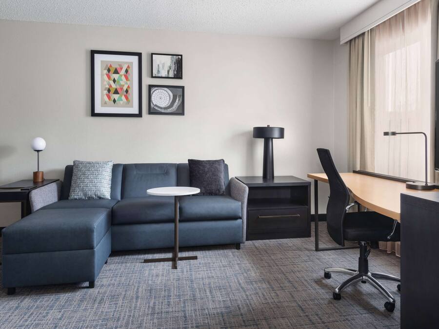 Habitación de hotel moderna con sofá, una mesita redonda, escritorio con silla y cuadros en la pared.
