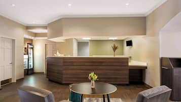 A modern hotel lobby with a reception desk, seating area, and a refrigerator with beverages.