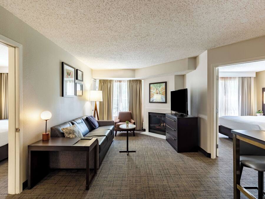 Habitación de hotel con sofá, televisor de pantalla plana, chimenea y zona de comedor.