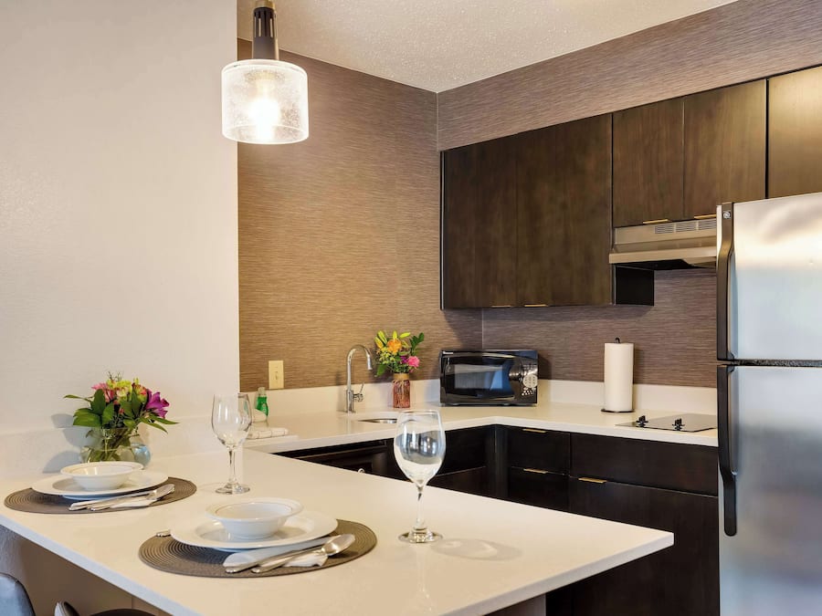 Une cuisine moderne dotée d’un îlot central, d’appareils électroménagers en acier inoxydable et d’un luminaire suspendu.