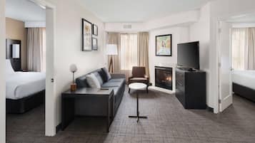 Quarto de hotel com cama, sofá, televisão, lareira e uma pequena mesa.