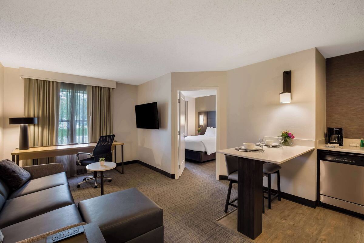 Ein Hotelzimmer mit Sofa, Schreibtisch, Bett, Fernseher und einer Küchenzeile.
