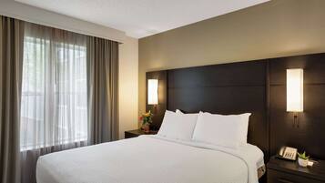 A hotel room with a large bed, a nightstand with a lamp, and a window with curtains.