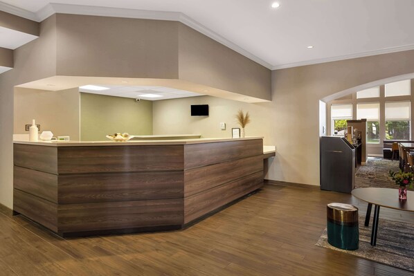 A modern reception area with a wooden counter, a flat-screen TV, and a large window providing natural light.