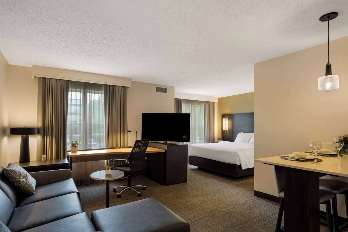 Ein Hotelzimmer mit Bett, Schreibtisch, Fernseher, Sofa und Esstisch.