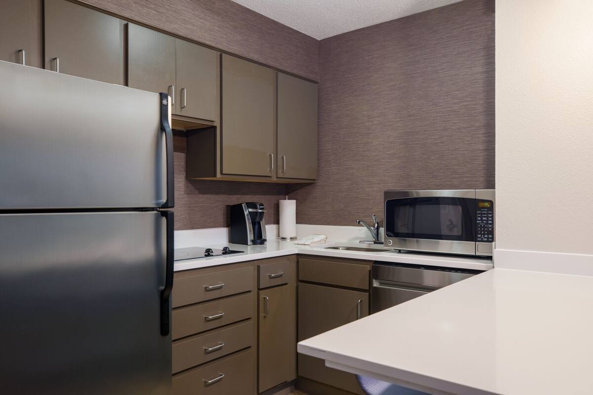 A modern kitchen with stainless steel appliances, wooden cabinets, and a white countertop.