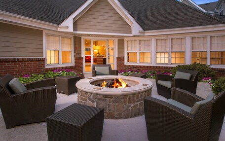 An outdoor patio with a stone fire pit surrounded by wicker furniture.