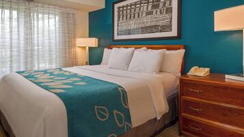 A hotel room with a bed, a wooden nightstand, a telephone, and a framed picture on the wall.