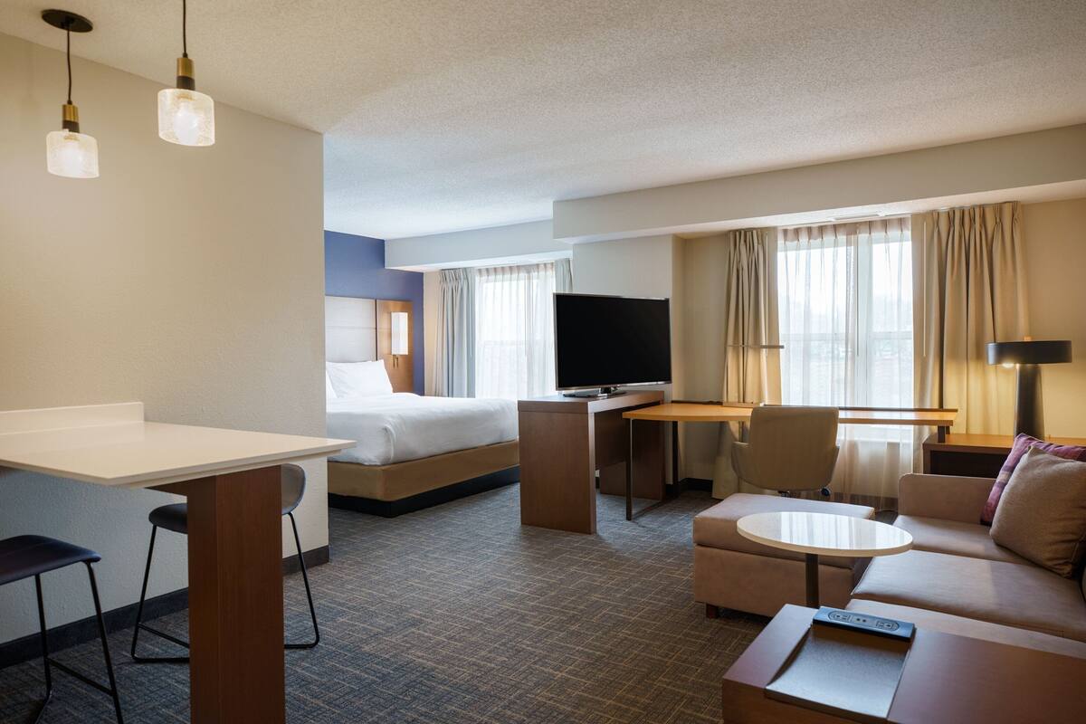 A hotel room with a bed, a desk, a TV, a sofa, and a dining table.