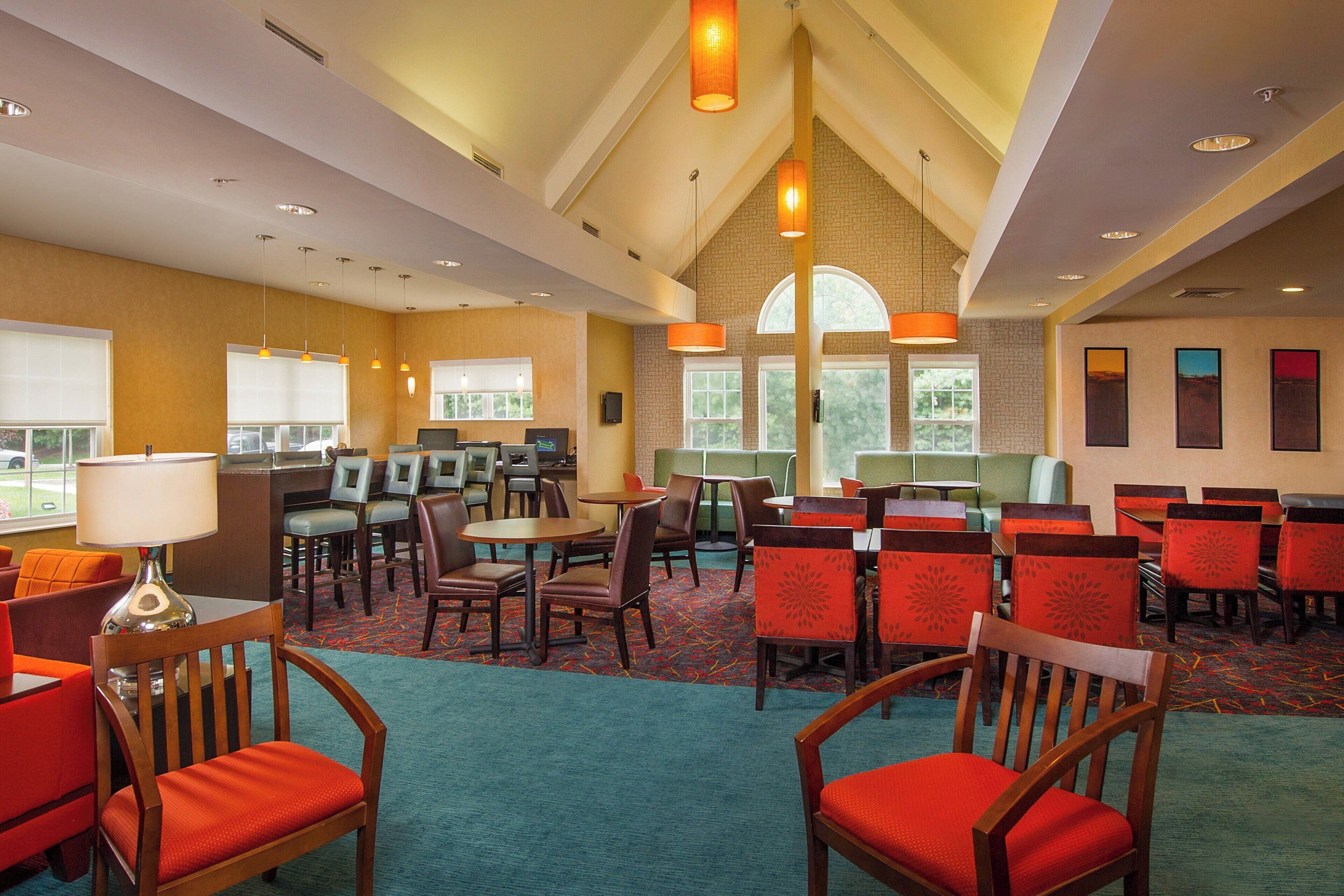 A hotel lobby with multiple seating areas, including tables and chairs, and a large window providing natural light.