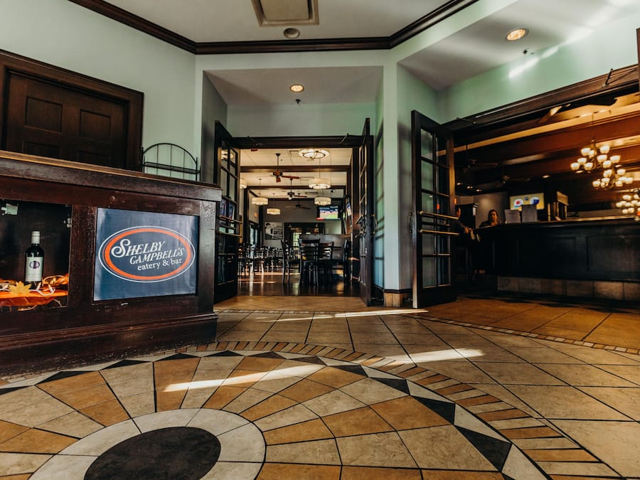A lobby with a reception desk, a bar area, and a tiled floor with a geometric pattern.