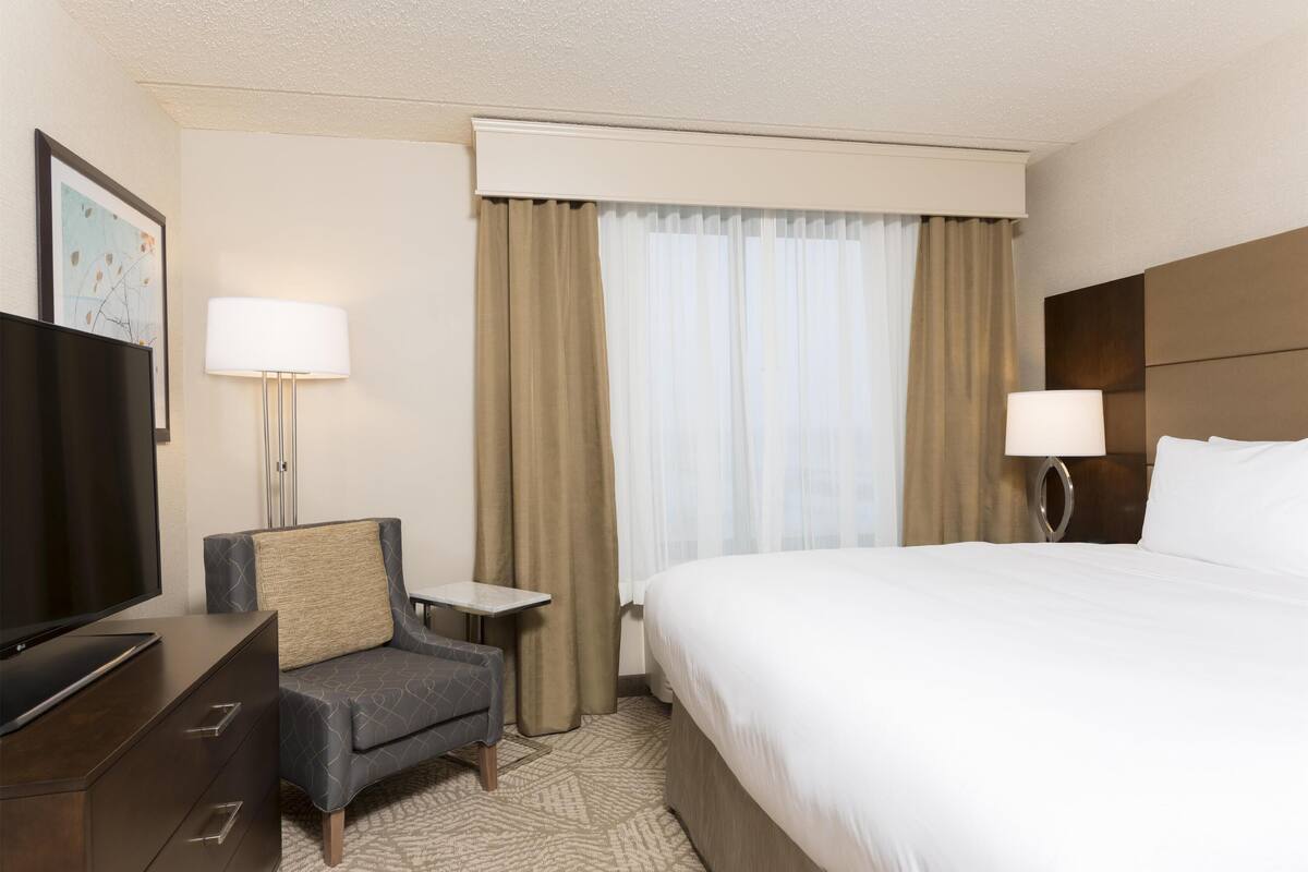 A hotel room with a bed, a TV, a small table, a chair, and a lamp.