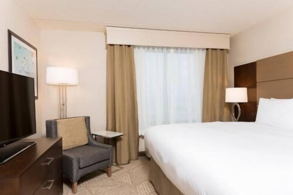 A hotel room with a bed, a desk, a chair, a television, and a window with curtains.