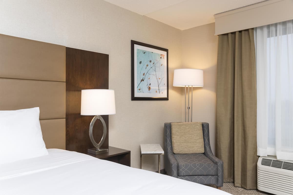 A hotel room with a bed, two bedside lamps, a chair, a small table, and a framed picture on the wall.