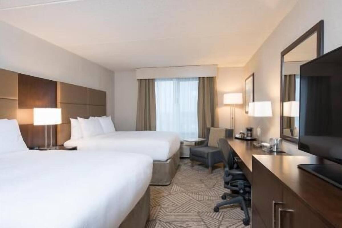 A hotel room with two beds, a desk, a chair, a TV, and a large mirror.