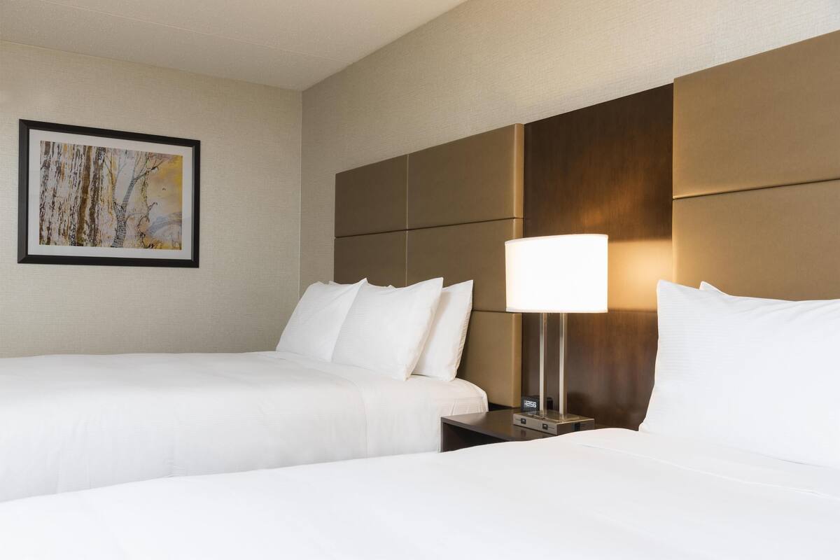 A hotel room with two beds, a nightstand, a lamp, and a framed picture on the wall.