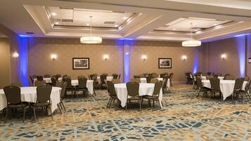 A conference room with multiple tables and chairs, ceiling lights, and framed pictures on the walls.