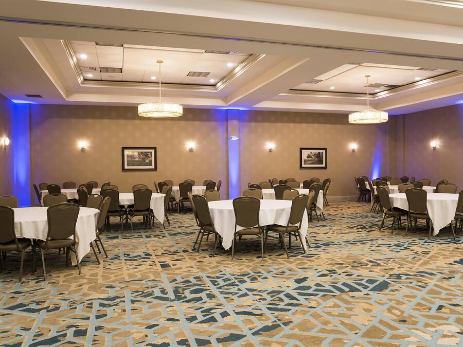 A conference room with multiple tables and chairs, ceiling lights, and framed pictures on the walls.