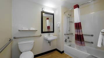 Un baño con inodoro blanco, lavamanos, espejo, ducha con cortina roja y blanca, y secador de manos.