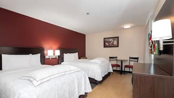 A hotel room with two beds, a desk, chairs, a lamp, and a framed picture on the wall.