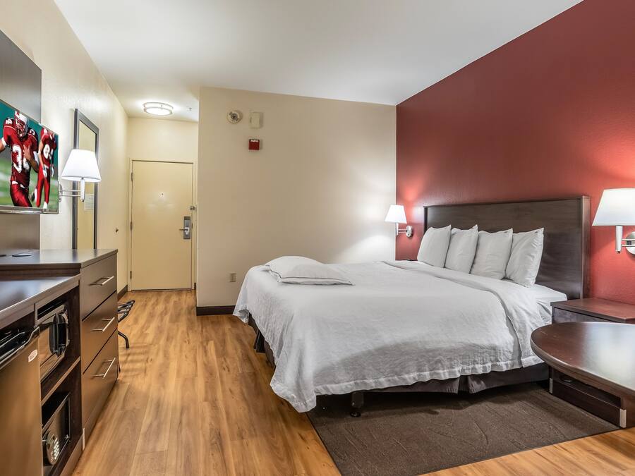 Quarto de hotel com cama, mesas de cabeceira, escrivaninha e televisão.