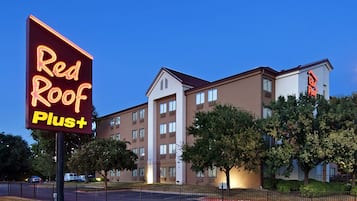 A Red Roof Plus hotel with a modern building facade, multiple windows, and a parking lot.