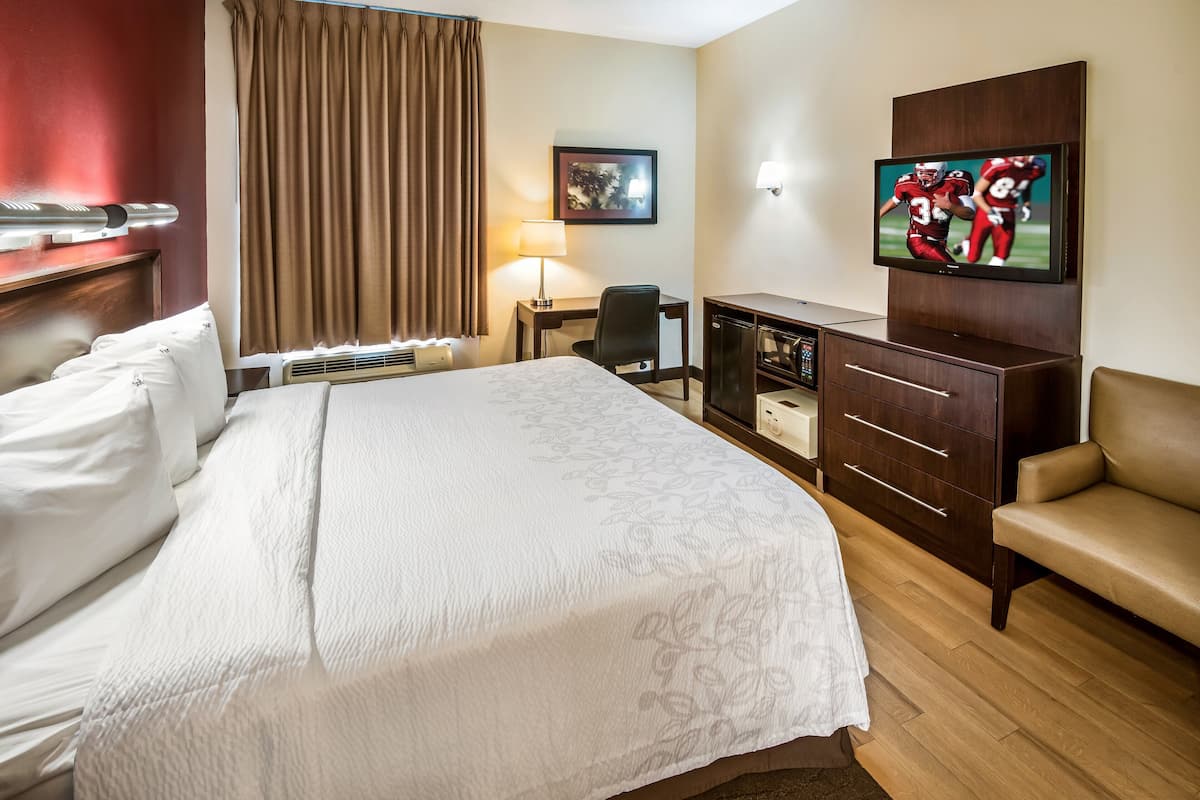 A hotel room with a large bed, a desk, a TV, and a seating area.