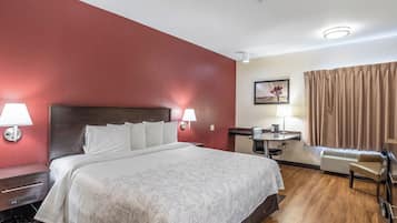 A hotel room with a bed, bedside lamps, a desk with a chair, a painting on the wall, and a window with curtains.