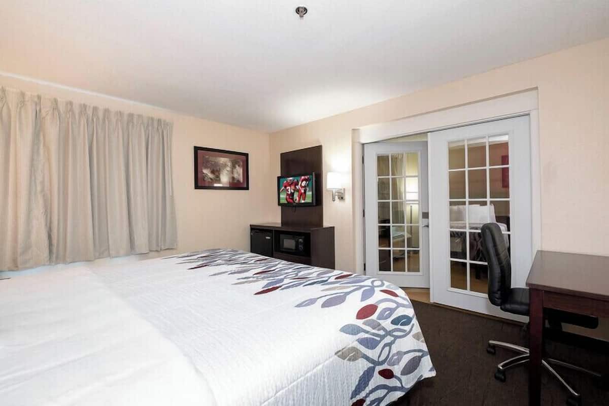 A hotel room with a large bed, a desk, a chair, a TV, and a sliding glass door to the outside.