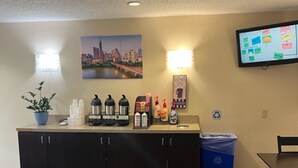 A reception area with a counter, a potted plant, a coffee station, a trash bin, and a TV screen.