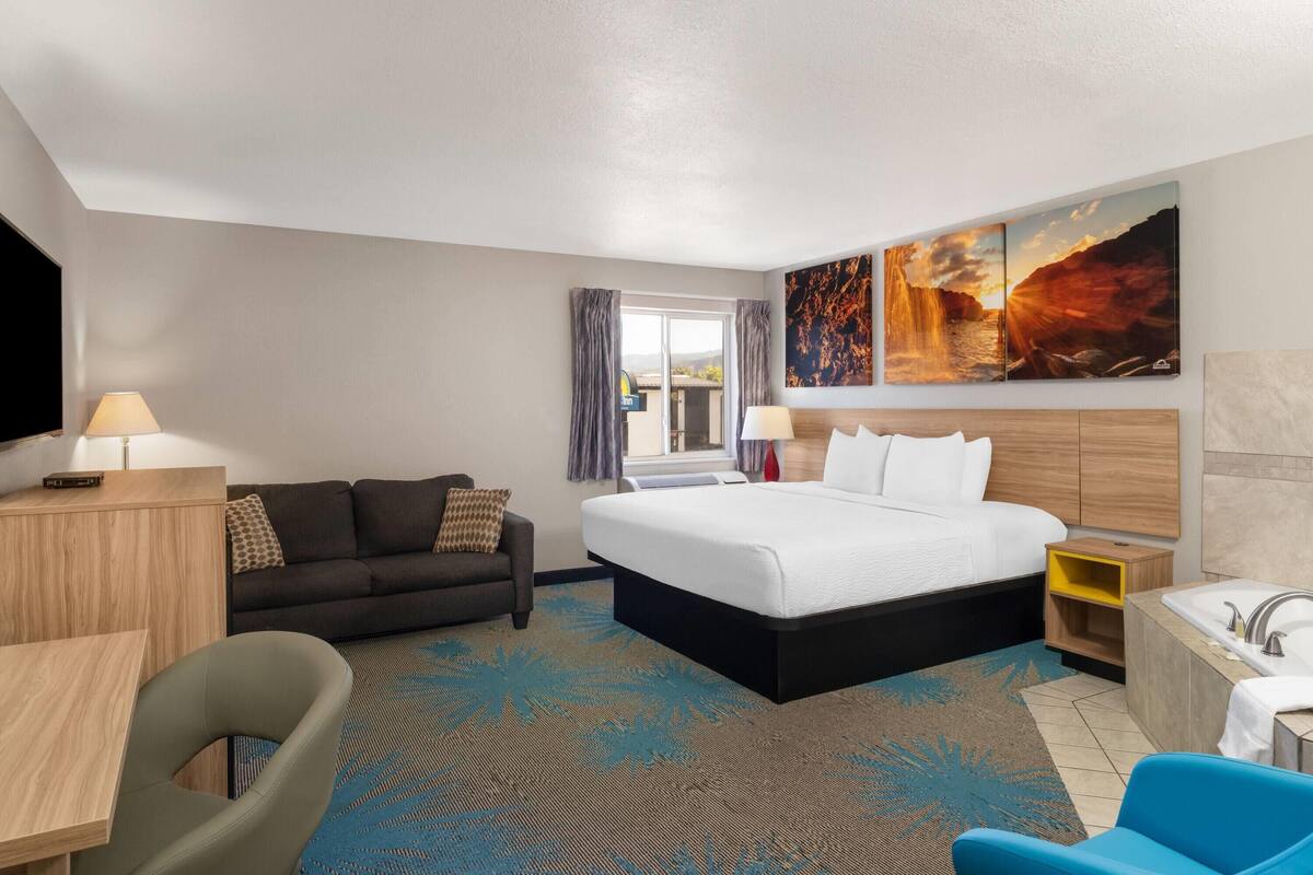 A hotel room with a large bed, a desk, a chair, a sofa, a bathroom with a bathtub, and a painting on the wall.