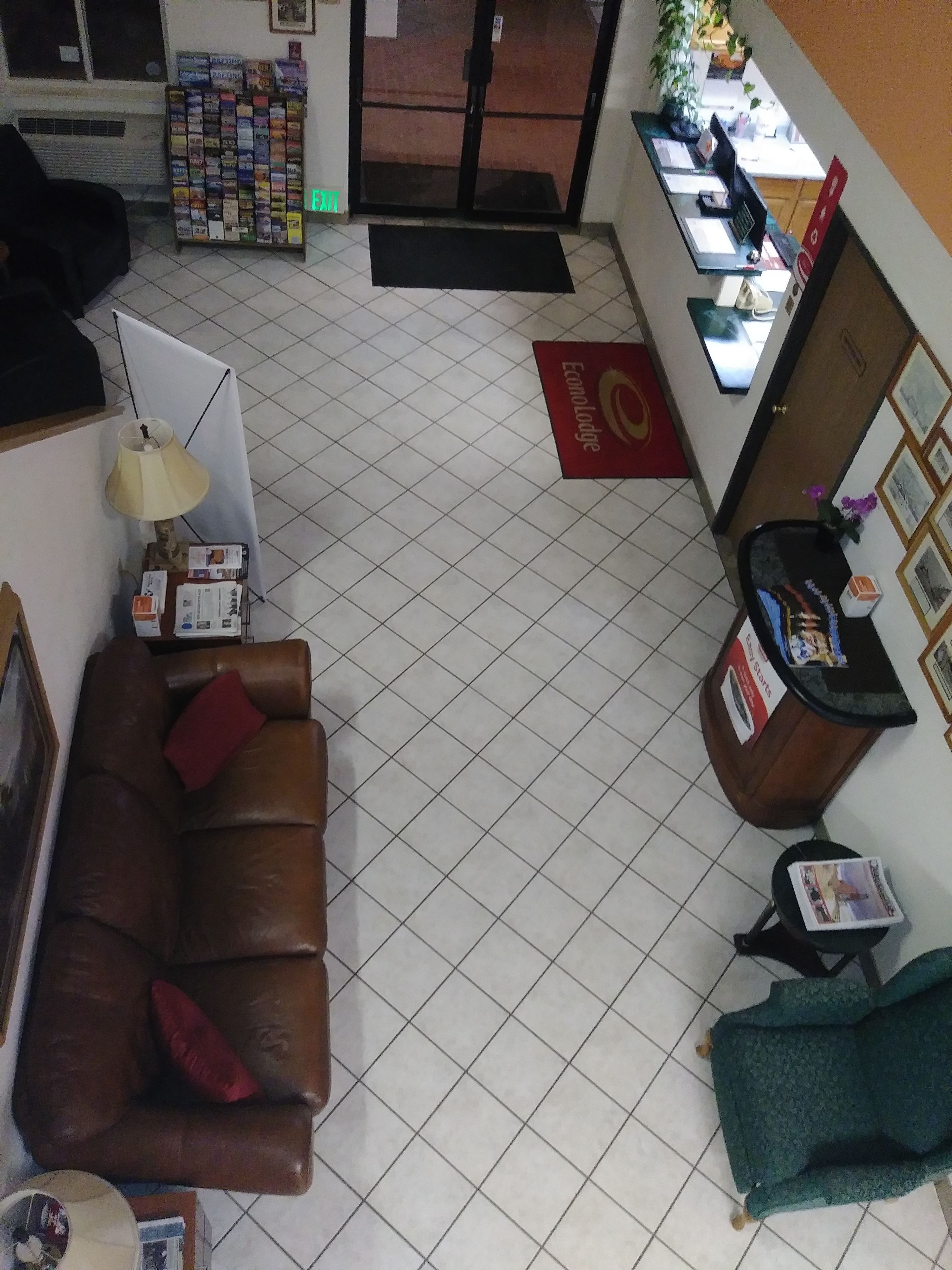 A reception area with a brown leather sofa, a green armchair, a desk with a computer, and a red carpet.