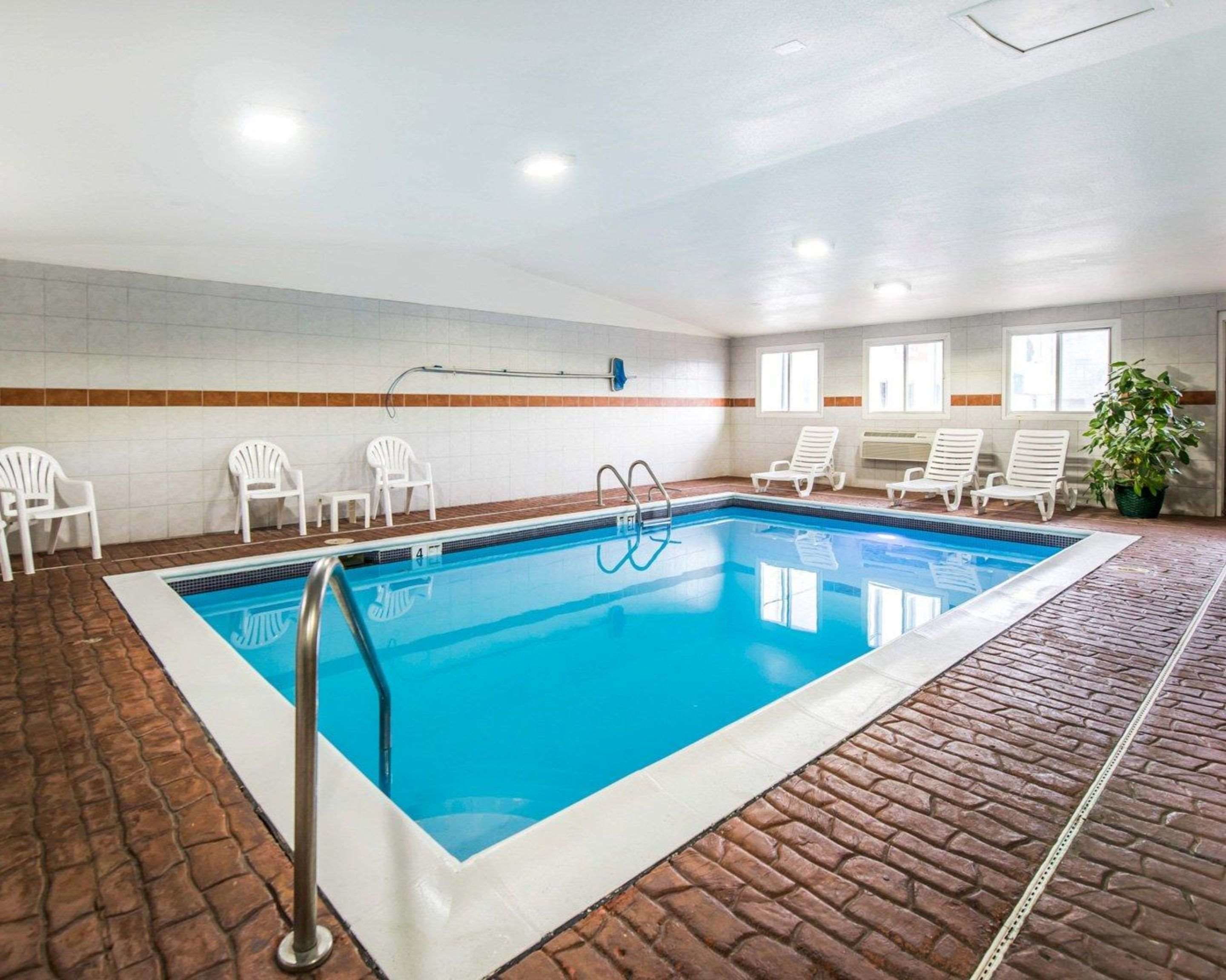 An indoor swimming pool with white lounge chairs and a potted plant.
