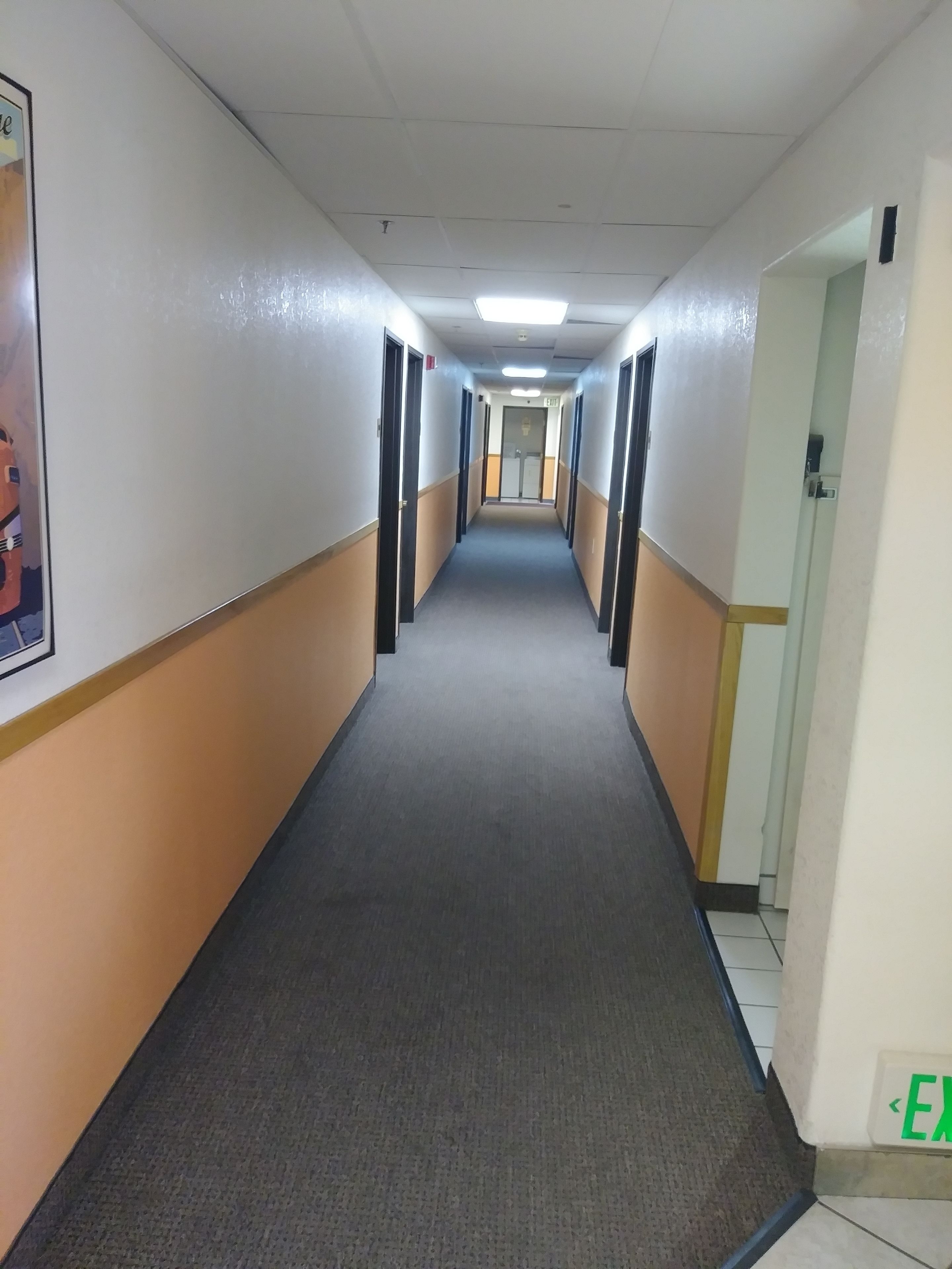 A long, narrow hallway with doors on both sides, a carpeted floor, and a tiled floor at the end.
