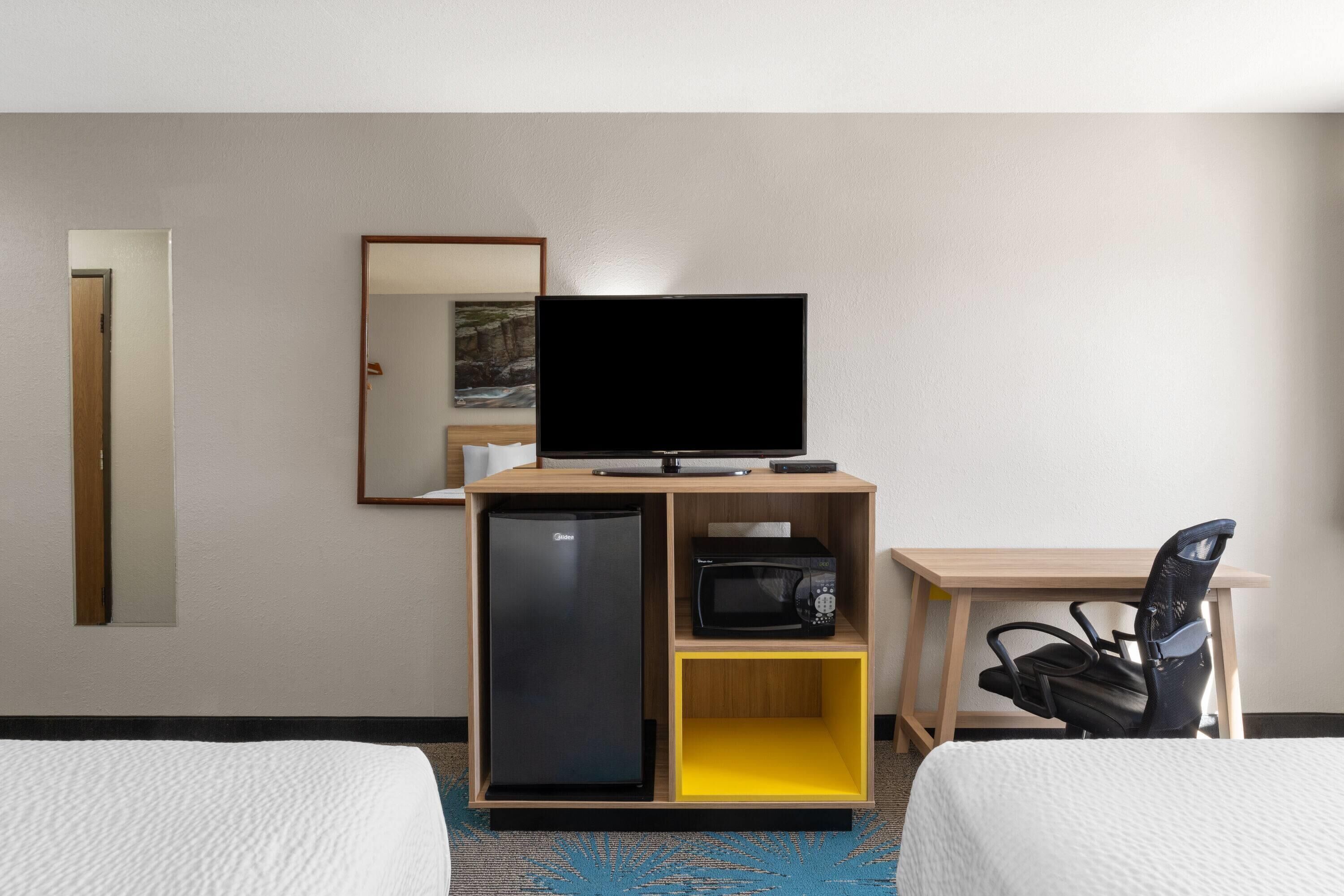 Una habitación de hotel con una cama, un televisor sobre un soporte de madera, un microondas y un refrigerador pequeño.