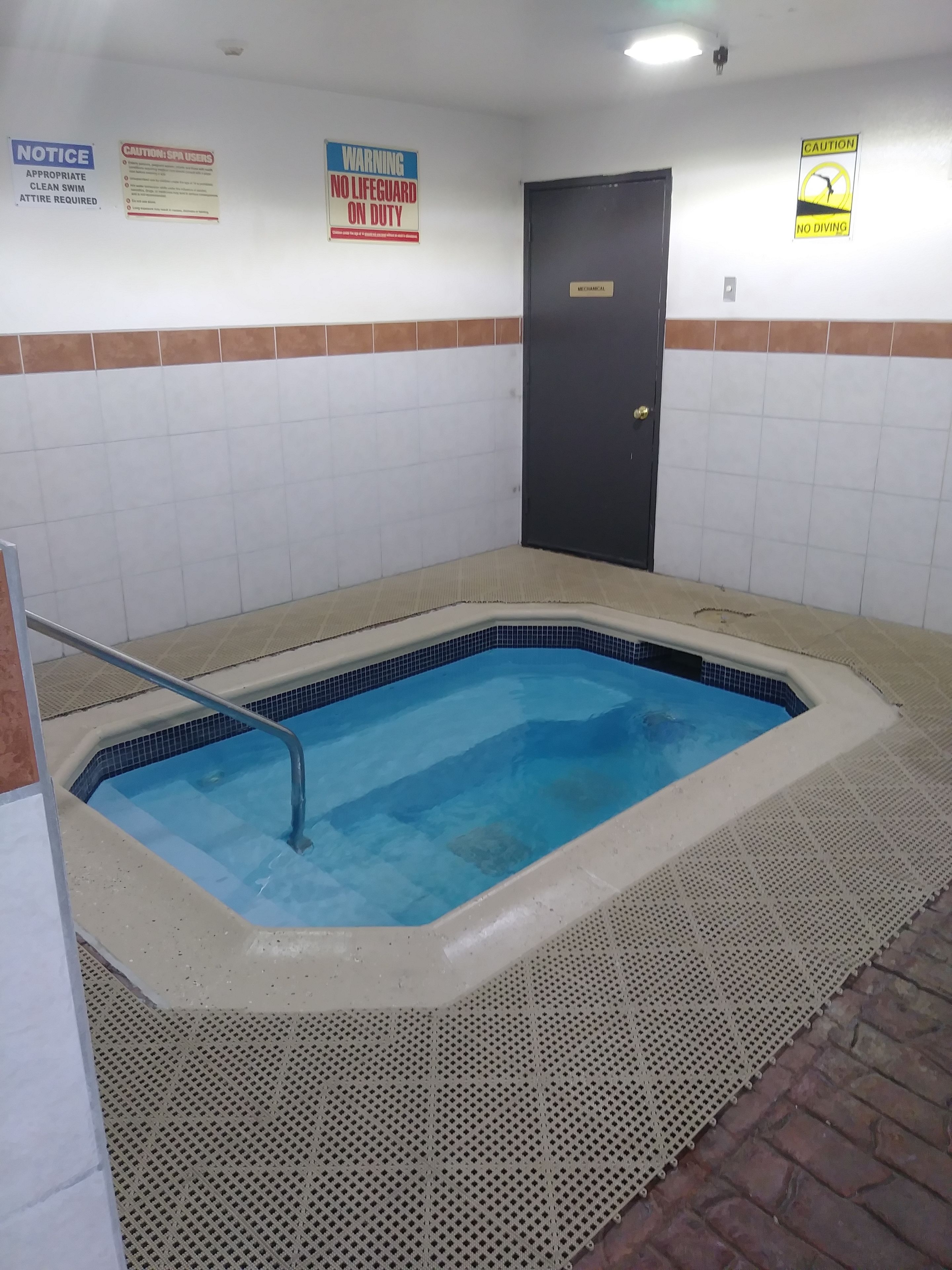 A small indoor pool with a tiled border, a metal ladder, and safety signs on the walls.