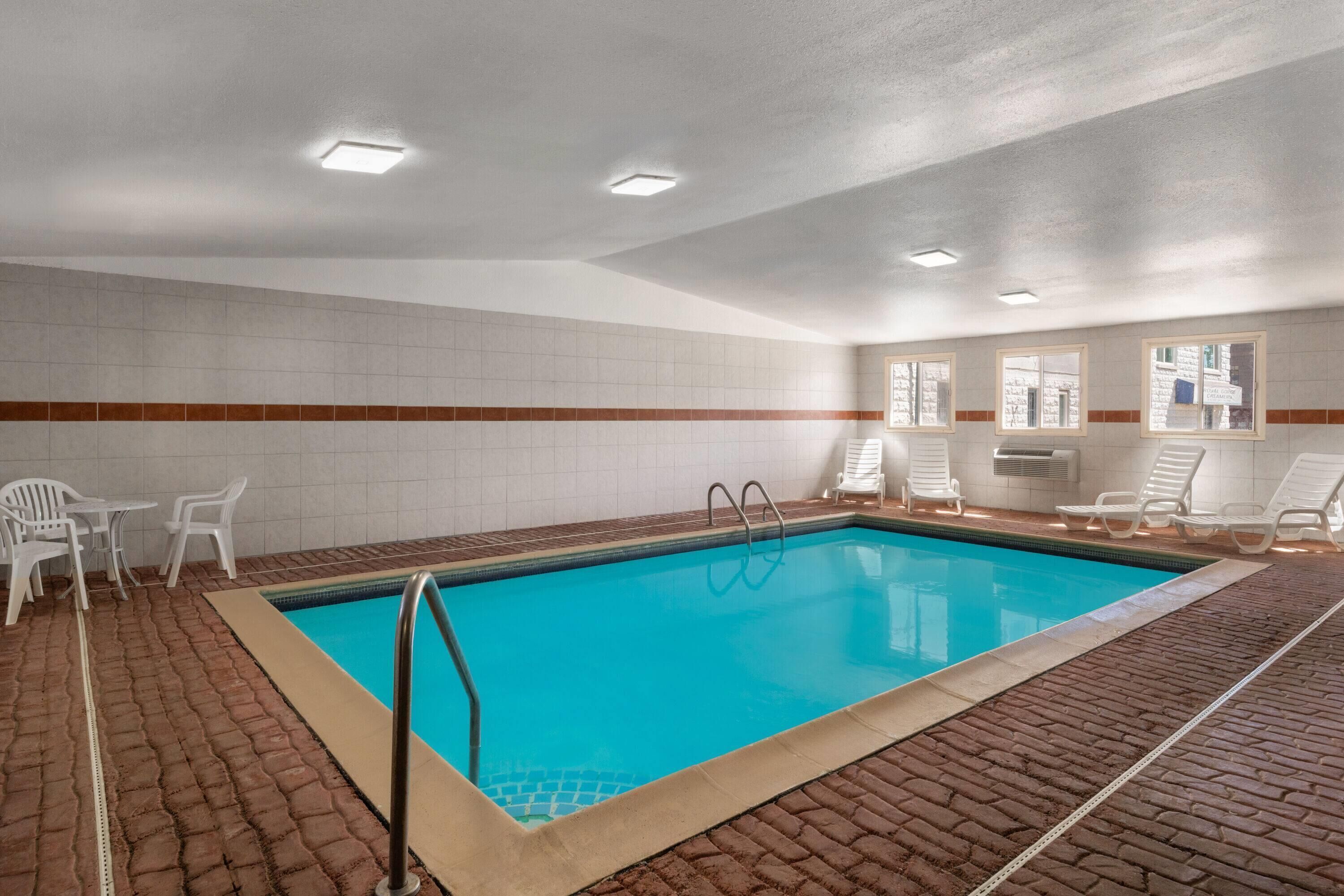 A swimming pool with clear blue water, surrounded by white lounge chairs and a tiled wall.