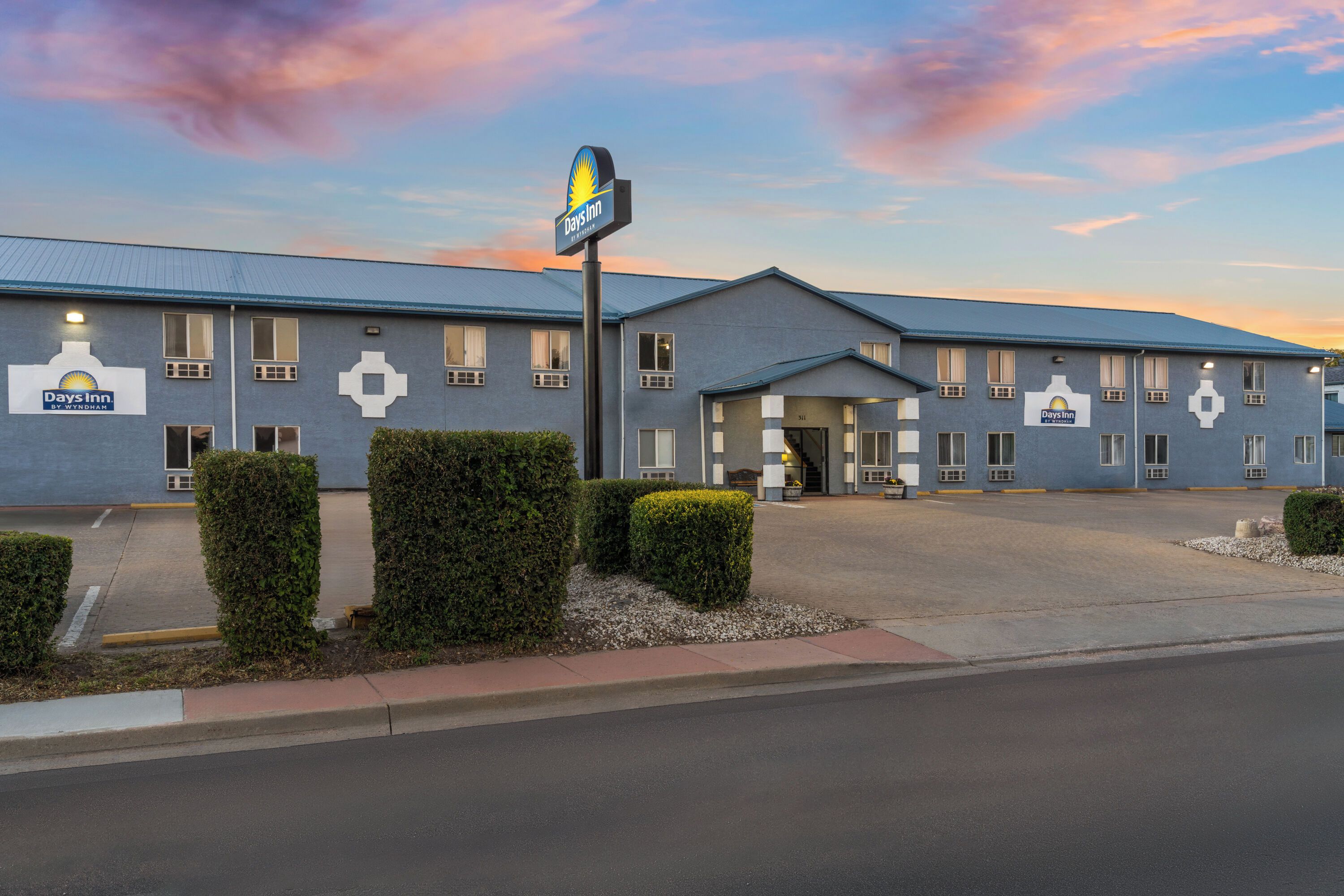 A Days Inn by Wyndham hotel with a simple, functional design, featuring a large parking lot and a clear sky.