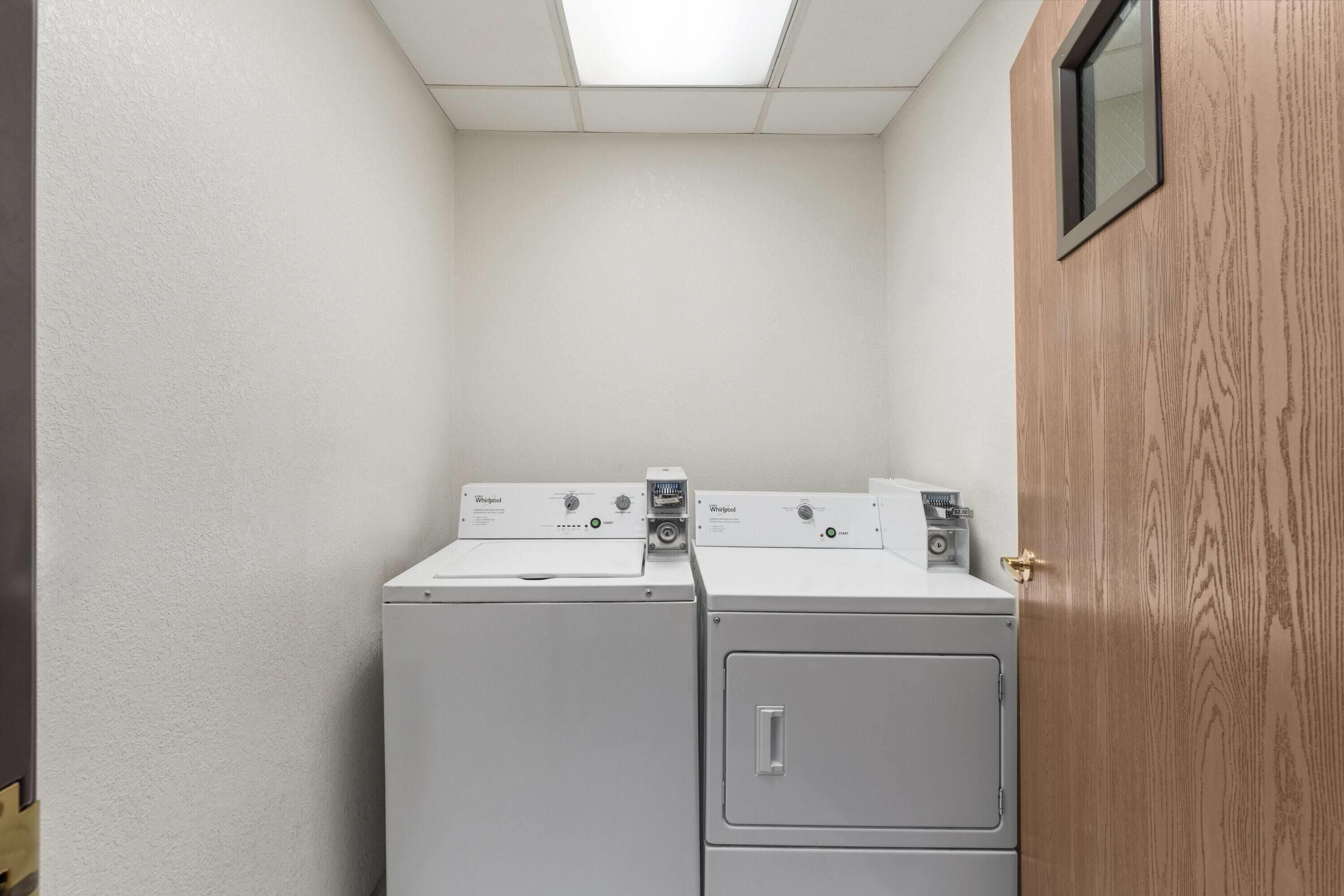 A laundry room with two stacked washers and a dryer, a wooden door, and a small window.