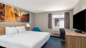 A hotel room with a large bed, a desk with a TV, a window with curtains, and a wall with three paintings.