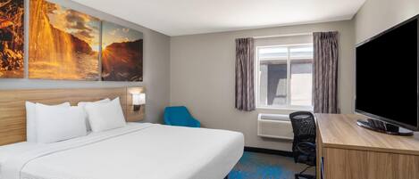 A hotel room with a large bed, a desk with a TV, a window with curtains, and a wall with three paintings.