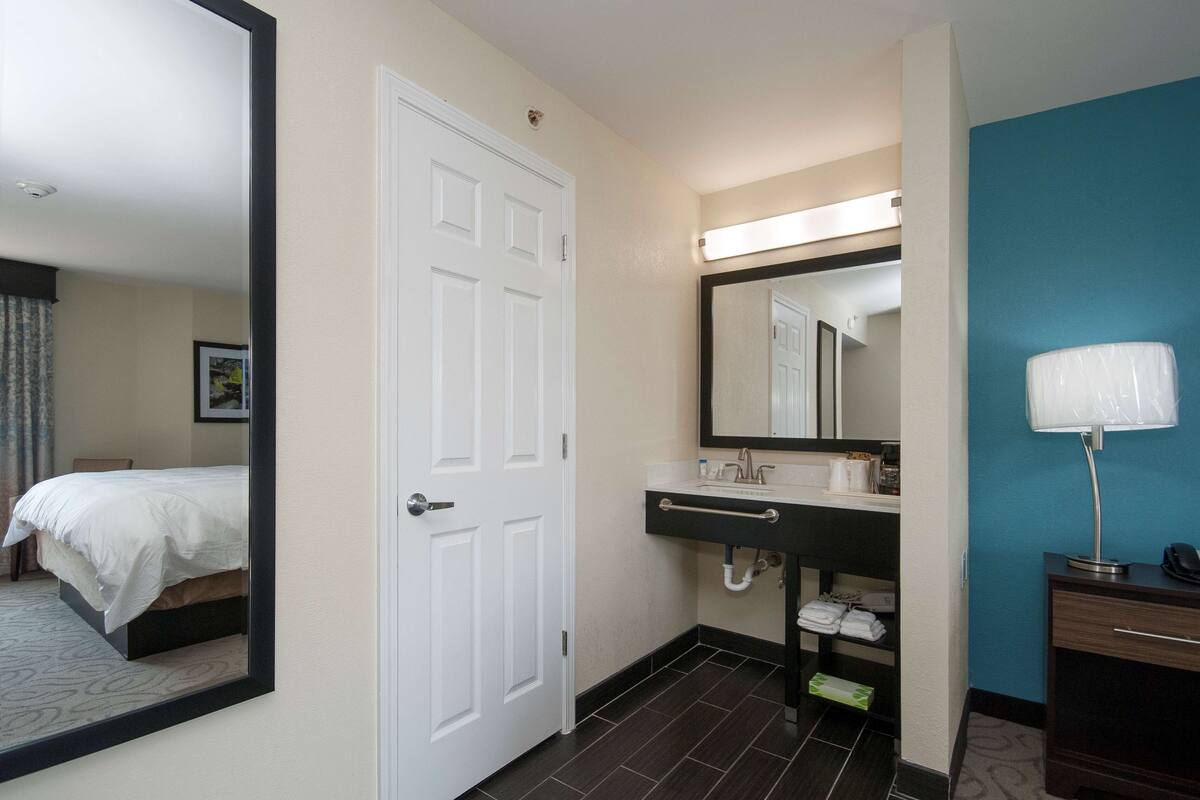 A hotel room with a bed, a bathroom with a sink, mirror, and towel rack.