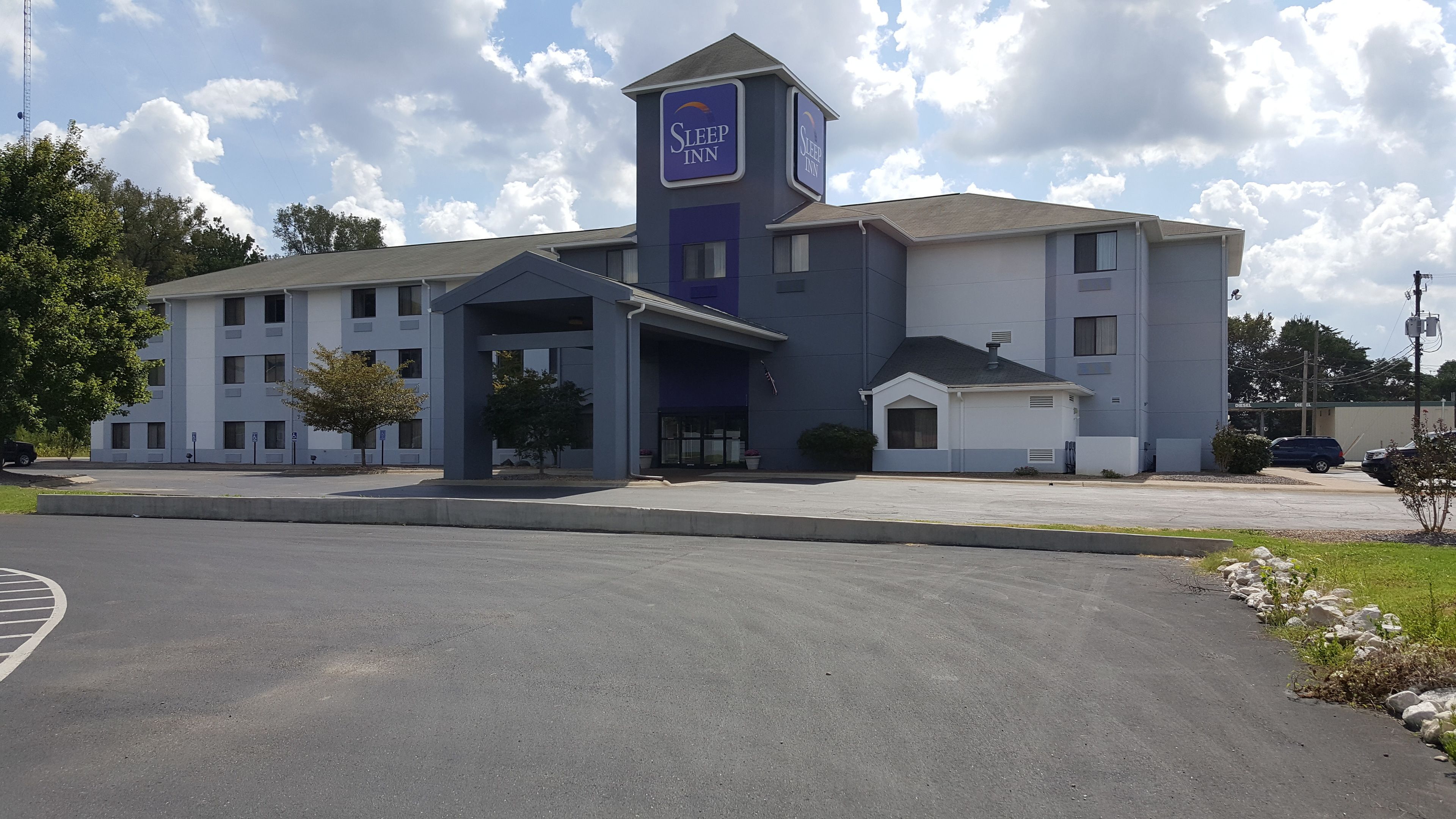 Un hotel Sleep Inn con un diseño moderno, que presenta una torre destacada con el logotipo de Sleep Inn, una entrada cubierta y un estacionamiento.