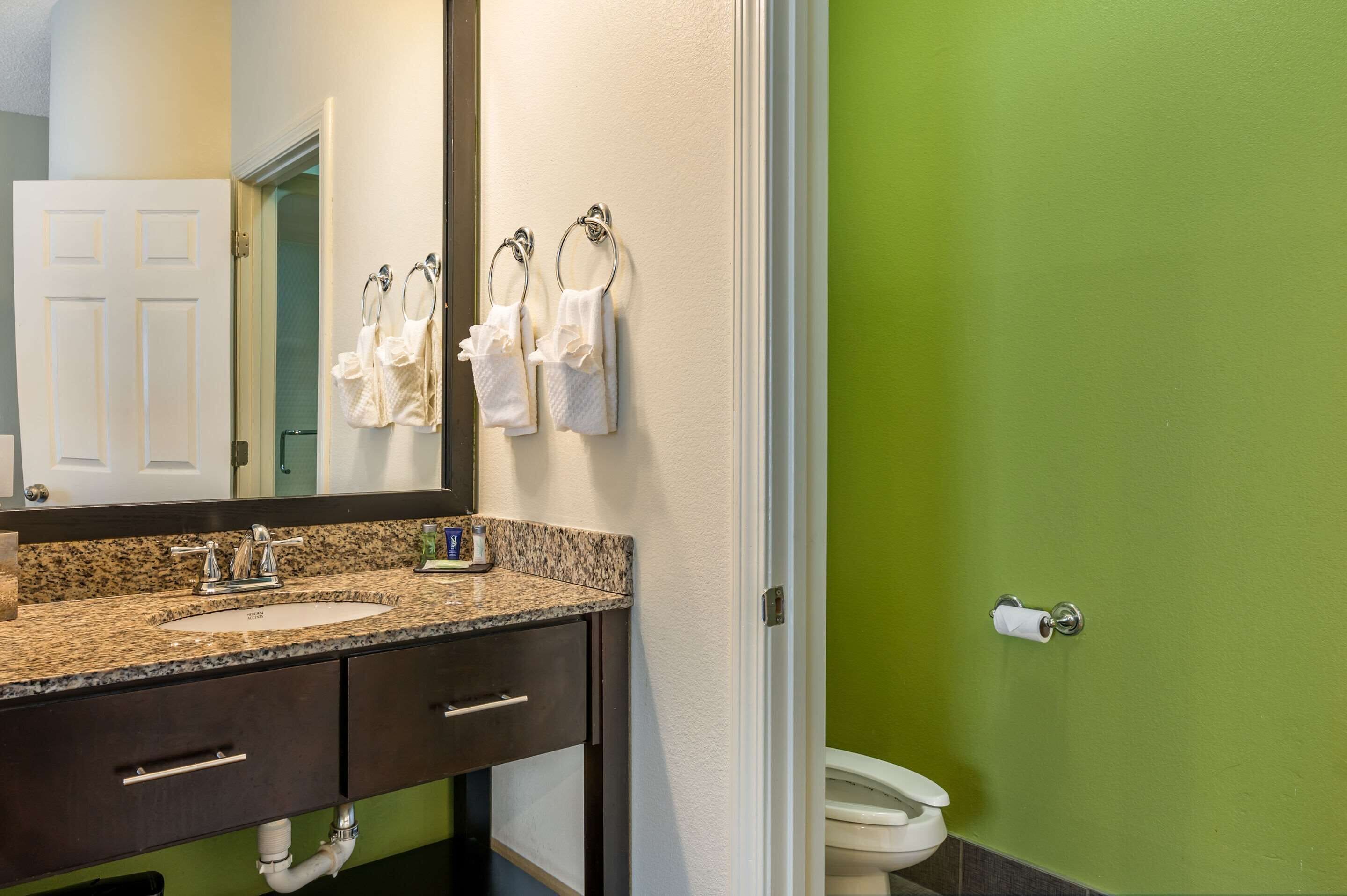 Une salle de bain avec un comptoir en granit, deux lavabos, un miroir et des toilettes.