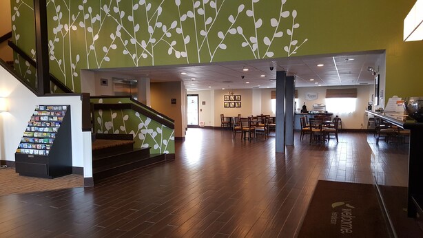 A spacious lobby with a wooden floor, a staircase with green walls and white leaf patterns, and a reception area with a counter and chairs. - Sleep Inn Henderson-Evansville South (Henderson)
