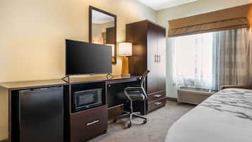 Habitación de hotel con cama, escritorio con televisor, lámpara, armario y ventana con cortinas.