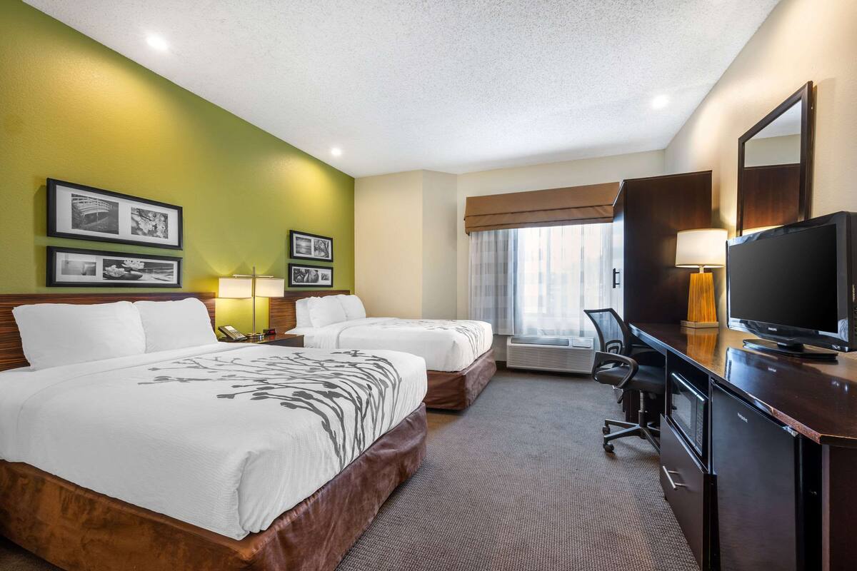 A hotel room with two beds, a desk with a TV, a lamp, and framed pictures on the wall.