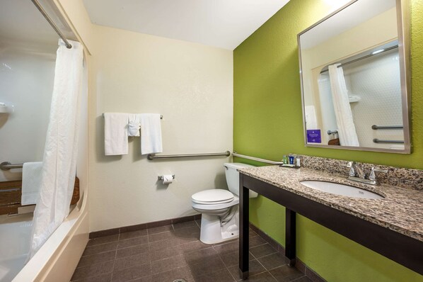 A bathroom with a white toilet, a sink with a granite countertop, a mirror, and a shower area with a white curtain. - Sleep Inn Henderson-Evansville South (Henderson)