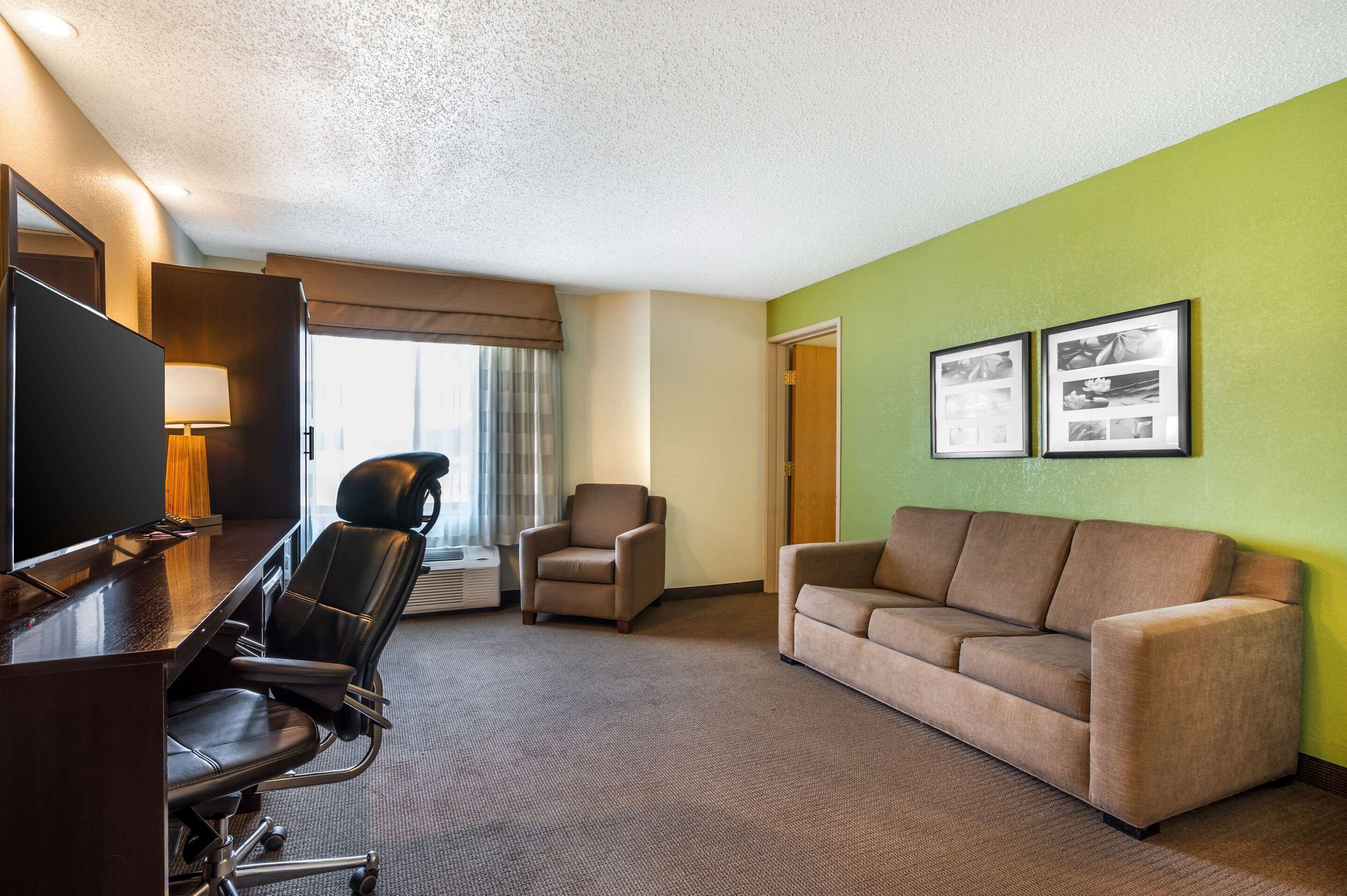 Habitación de hotel con escritorio, dos sillas, un sofá, un televisor y cuadros en la pared.
