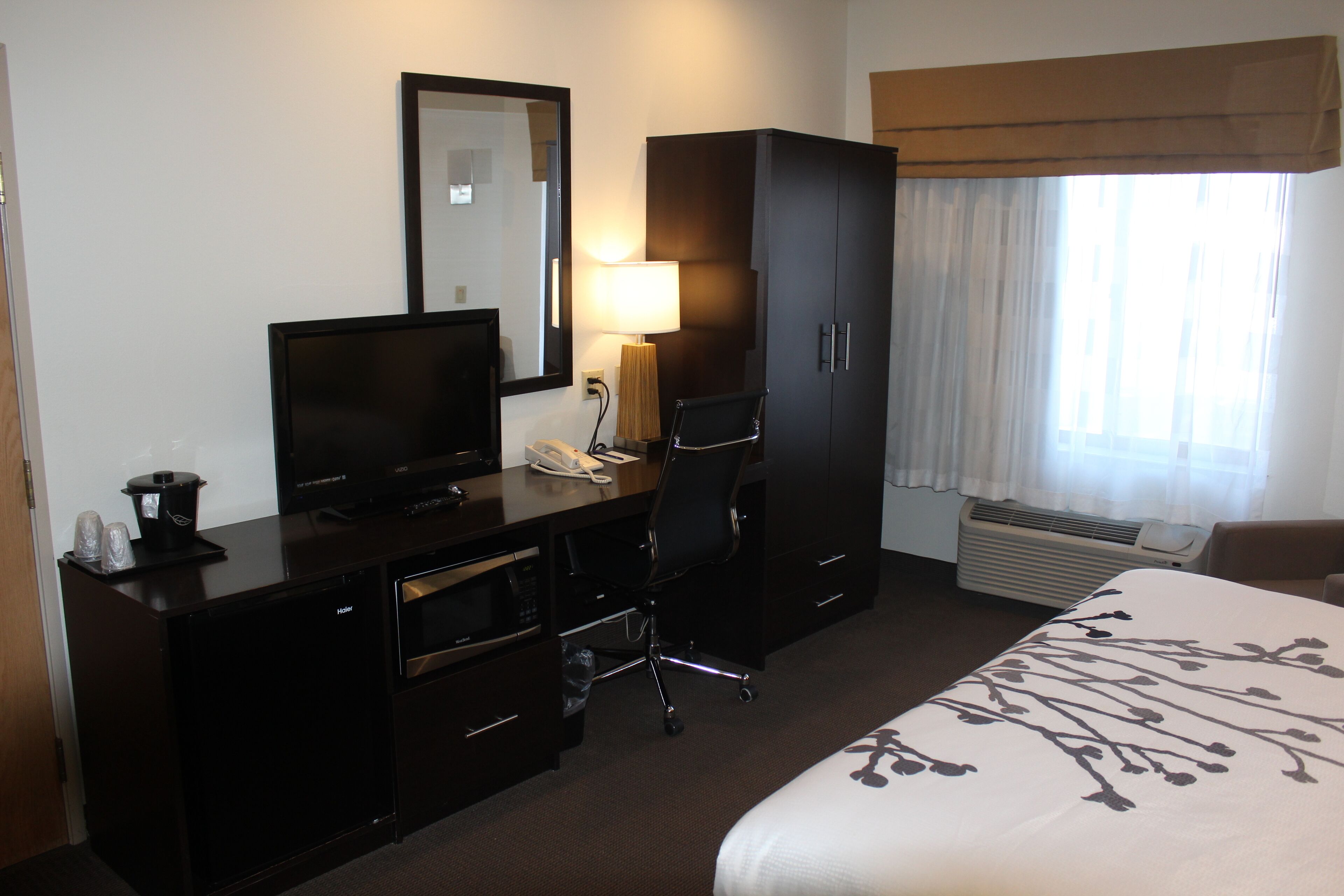 Habitación de hotel con cama, escritorio con computadora, televisor, armario y ventana con cortinas.